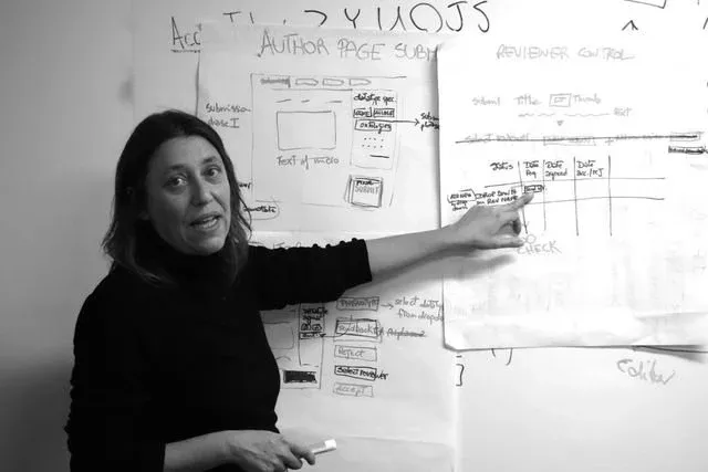 A sprint participant points to hand-drawn flipchart sheets mapping a publishing workflow, with sketched screens labelled ‘AUTHOR PAGE SUBMIT’ and a ‘REVIEWER CONTROL’ table of submission, title, date and decision columns.